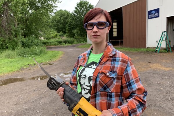 A woman wearing safety glasses and holding a saw